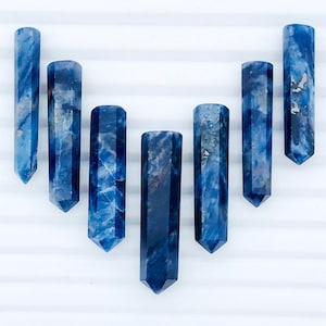 Può includere: Sette punte di pietre preziose blu e bianche disposte a forma di cuore su uno sfondo bianco.