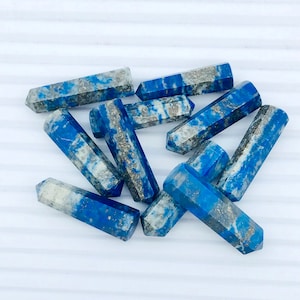 May include: A group of ten blue and white lapis lazuli crystal points. The points are smooth and polished, with a natural, irregular shape. The points are arranged in a random pattern on a white surface.