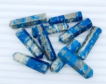 Könnte beinhalten: Zehn blaue und weiße Lapislazuli-Kristallspitzen. Die Spitzen sind glatt und poliert, mit einer natürlichen, unregelmäßigen Form. Die Spitzen sind in einem zufälligen Muster auf einer weißen Oberfläche angeordnet.