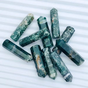 May include: A collection of ten green, white, and brown agate crystal points. The points are all roughly the same size and shape, and they are arranged in a pile on a white surface.