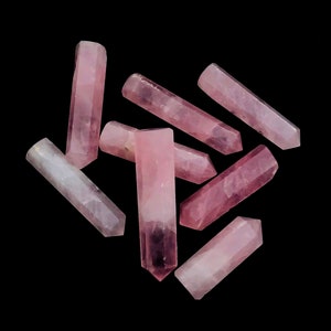 Pode incluir: Um grupo de sete varinhas de cristal rosa, também conhecidas como pontas, estão espalhadas sobre um fundo preto. As varinhas são de tamanhos e formas diferentes, mas todas têm uma ponta pontiaguda e uma superfície lisa e polida.