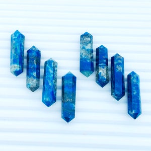 May include: Seven blue lapis lazuli crystal points, each with a unique shape and pattern, arranged in a staggered formation on a white background.