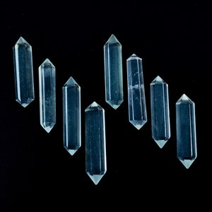 Może przedstawiać: Osiem przezroczystych, fasetowanych kryształowych punktów, znanych również jako różdżki lub wieże, ułożonych w przesunięty wzór na czarnym tle. Kryształy są półprzezroczyste i mają lekko zielony odcień.