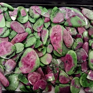 May include: A collection of green and pink gemstone cabochons in various shapes and sizes. The stones have a mottled appearance with green, pink, and black markings.