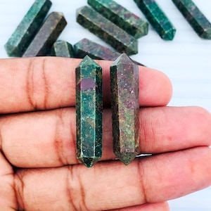 May include: Two green and red gemstone points, also known as ruby in zoisite, are held in a hand. The points are approximately 2 inches long and have a pointed tip.