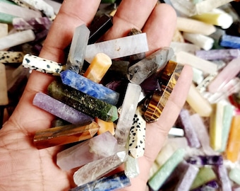 May include: A hand holding a variety of small, polished gemstone points. The points are in various colors, including clear, white, purple, blue, green, brown, and orange. The points are all about 1-2 inches long.