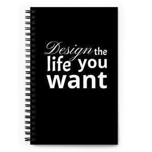 May include: A black spiral-bound notebook featuring the white text "Design the life you want" printed on the front cover. The notebook has a vertical black metal coil binding along the left side and a solid black background with white lettering.