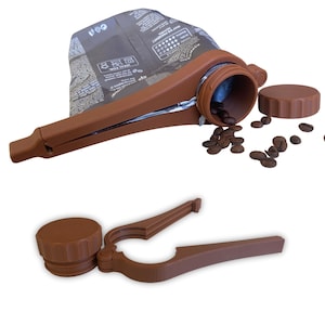 Puede incluir: Un clip y dispensador de bolsa de café marrón con una tapa a juego. El clip sujeta una bolsa de granos de café, con algunos granos derramándose. El clip es de plástico y tiene una palanca para abrirlo y cerrarlo.