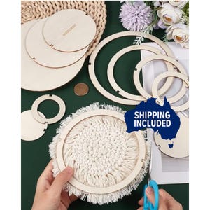 May include: A selection of unfinished wooden craft supplies, including circular frames, discs, and a macrame coaster. The items are arranged on a green surface with a woven placemat and flowers in the background. A pair of scissors is also present.