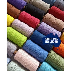 May include: A selection of macrame cord spools in a variety of colours, such as purple, black, red, and blue. The spools are neatly arranged, displaying the range of colours suitable for craft projects.