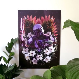 Peut inclure: Un Mandalorien violet et argenté avec une lance et une petite créature verte dans une couronne de fleurs. L'arrière-plan est sombre avec des fleurs roses et rouges.
