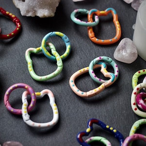 Könnte beinhalten: Sortiment aus bunten, gemusterten, miteinander verbundenen Metallringen. Die Ringe haben verschiedene Formen, darunter Kreise, Ovale und Herzen. Die Ringe sind miteinander verbunden und bilden Ketten.