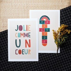 May include: Two cards, one with the text 'JOLIE COMME UN COEUR' in colorful letters and the other with a hopscotch game with numbers 1 through 8 in a rainbow design.