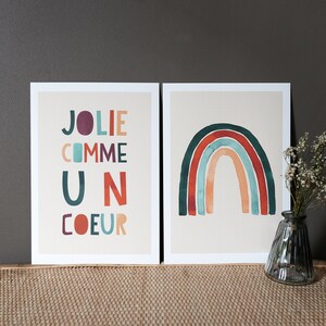 May include: Two framed prints, one with a rainbow in shades of red, orange, yellow, green, blue, and purple, and the other with the text 'JOLIE COMME UN COEUR' in colorful letters.