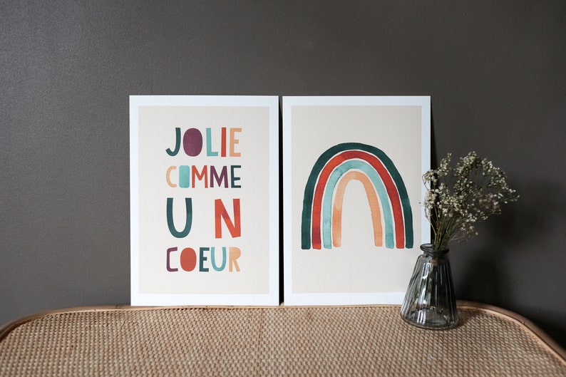 May include: Two framed prints, one with a rainbow in shades of red, orange, yellow, green, blue, and purple, and the other with the text 'JOLIE COMME UN COEUR' in colorful letters.
