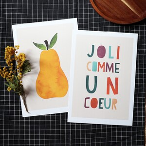 May include: Two printable art prints. The first print features a yellow pear with a green stem and leaves. The second print features the text 'JOLI COMME UN COEUR' in colorful, stylized letters.