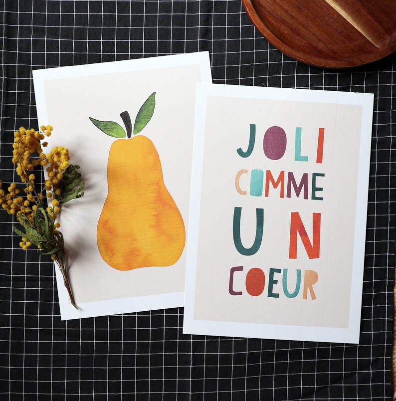 May include: Two printable art prints. The first print features a yellow pear with a green stem and leaves. The second print features the text 'JOLI COMME UN COEUR' in colorful, stylized letters.