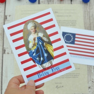May include: A white card with red and white stripes. A portrait of Betsy Ross sewing the first American flag is in the center of the card. The text "Betsy Ross 1752-1836" is at the bottom of the card.