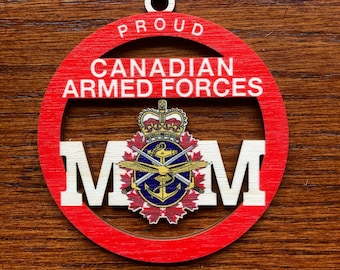 Op de afbeelding: Rode houten ornament met een witte cirkel in het midden. De cirkel heeft de tekst "PROUD CANADIAN ARMED FORCES" rond de rand en de letters "MOM" aan weerszijden van het wapen van de Canadese strijdkrachten.