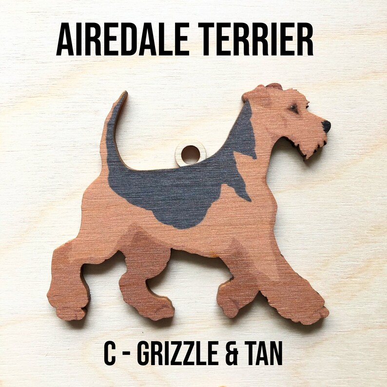 May include: A wooden cutout of an Airedale Terrier dog in a grizzle and tan color scheme. The dog is standing on all four legs with its tail curled up. The cutout is labeled "C - Grizzle & Tan".