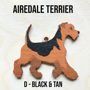 May include: A wooden cutout of an Airedale Terrier dog in black and tan colors. The cutout is a decorative ornament with a hole for hanging. The text "D - BLACK & TAN" is printed below the dog.