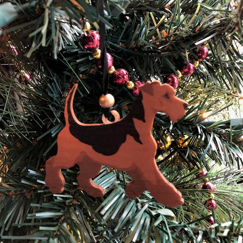 May include: A wooden Christmas ornament shaped like an Irish Terrier dog. The ornament is brown and black with a gold bead hanging from the top.