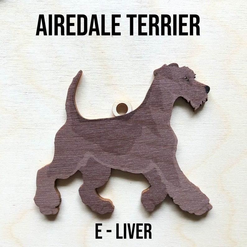 May include: A wooden cutout of an Airedale Terrier dog in a brown color. The dog is standing on all four legs with its head turned to the side. The text "Airedale Terrier" is printed above the dog and "E - Liver" is printed below the dog.