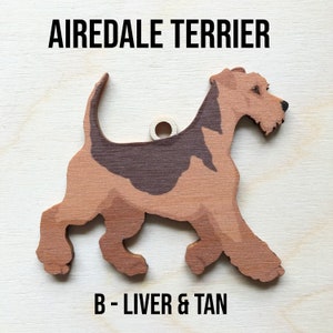 May include: A wooden cutout of an Airedale Terrier dog in a liver and tan color. The dog is walking and has a hole in the top for hanging. The text "Airedale Terrier" and "B - Liver & Tan" are printed below the dog.