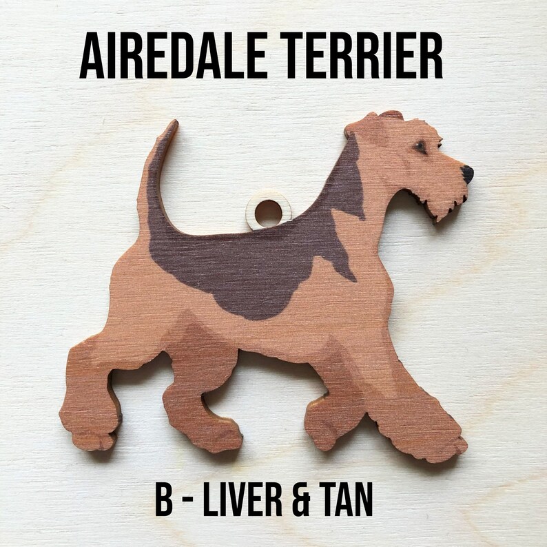 May include: A wooden cutout of an Airedale Terrier dog in a liver and tan color. The dog is walking and has a hole in the top for hanging. The text "Airedale Terrier" and "B - Liver & Tan" are printed below the dog.