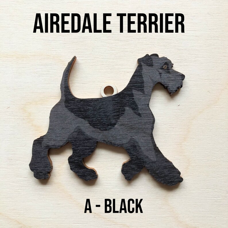 May include: A black wooden Airedale Terrier dog ornament. The ornament is a silhouette of a dog with a hole at the top for hanging. The text "A - BLACK" is printed below the ornament.