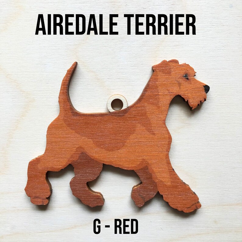 May include: A red wooden Airedale Terrier dog ornament with a hole for hanging. The ornament is painted with a realistic design and has the text "G - RED" printed below it.