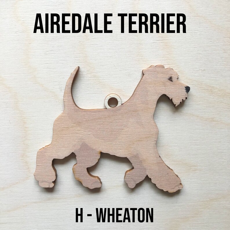 May include: A wooden cutout of an Airedale Terrier dog, painted in a light brown color. The cutout is labeled "H - WHEATON" at the bottom.