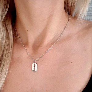 Könnte beinhalten: Eine silberne Kettenkette mit einem Rasiermesser-Anhänger.