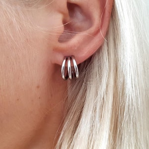 May include: Silver hoop earrings with three stacked rings. The earrings are worn in the left ear.