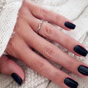 May include: A hand with black nail polish on each finger. The hand is wearing a silver ring on the ring finger.