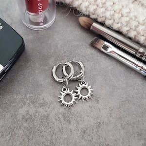 Pode incluir: Brincos de argola de prata com um pequeno charme de sol pendurado em cada argola.