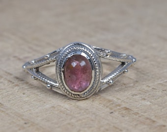 May include: A silver ring with a pink oval gemstone set in a delicate, ornate design.