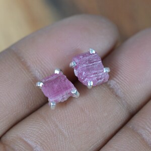 May include: A pair of silver earrings featuring pink tourmaline gemstones. The gemstones are raw and have a natural, irregular shape.