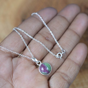 Peut inclure: Un collier en argent avec un pendentif rond orné d'une pierre précieuse verte et rose.