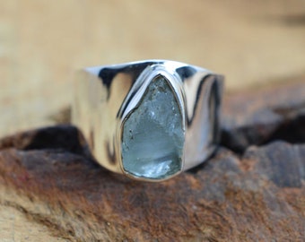 May include: A silver ring with a light blue aquamarine gemstone. The ring has a wide band and the gemstone is set in a bezel setting.