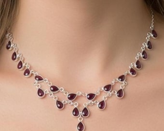 May include: A silver necklace with a cascading design featuring teardrop-shaped, deep red gemstones. The necklace has multiple strands that gracefully drape across the neckline, creating an elegant and eye-catching accessory.