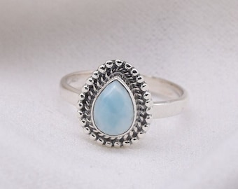 May include: A silver ring featuring a light blue teardrop-shaped gemstone set in a beaded bezel.