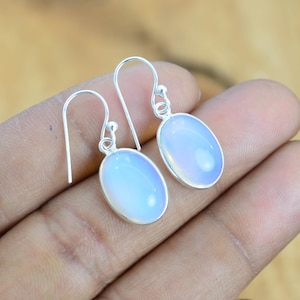 May include: A pair of silver dangle earrings with oval-shaped opal stones. The stones are a pale blue color with a slight iridescent shimmer.