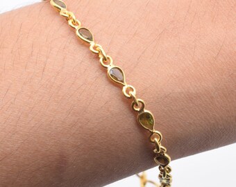 May include: A gold chain bracelet with green gemstone accents. The bracelet features a delicate chain with small, teardrop-shaped gemstones.