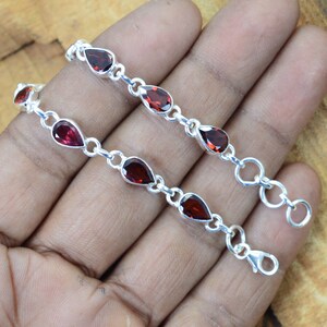 May include: A silver chain bracelet with red gemstone teardrop-shaped beads. The bracelet has a lobster clasp closure.