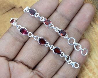 May include: A silver chain bracelet with red gemstone teardrop-shaped beads. The bracelet has a lobster clasp closure.