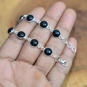 May include: A silver bracelet with black gemstone beads. The bracelet has a lobster clasp closure.