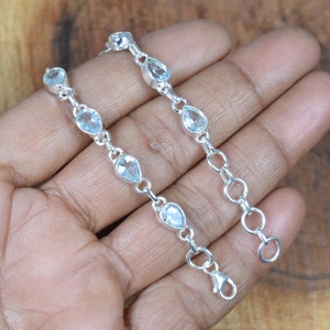 May include: A silver chain bracelet with teardrop-shaped blue topaz gemstones. The bracelet has a lobster clasp closure.