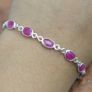 May include: A silver bracelet with pink oval-shaped gemstones. The bracelet is on a person's wrist.