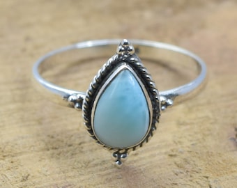 May include: A teardrop-shaped blue gemstone ring set in a silver band with a delicate rope design.